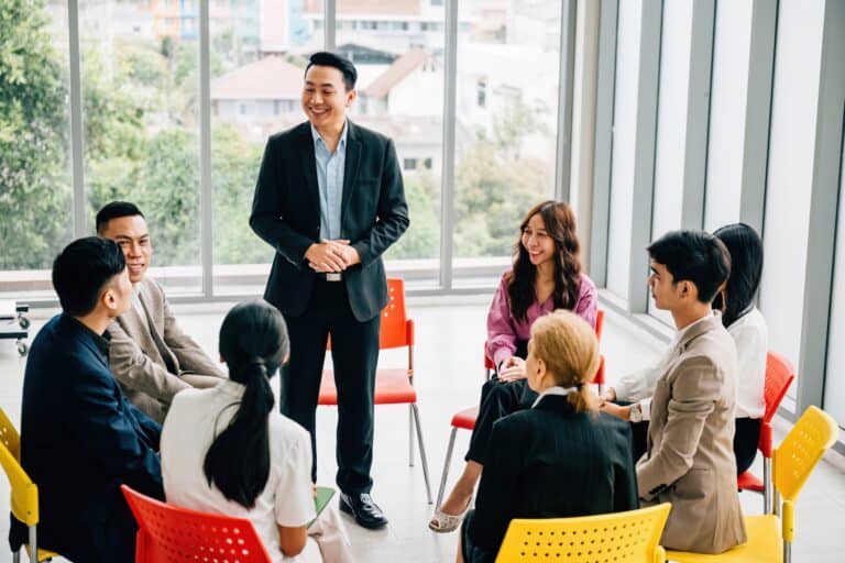 A diverse team of business professionals collaborates in a modern office. They engage in planning, explaining, and presenting, showcasing teamwork, diversity, and confidence in a business meeting.